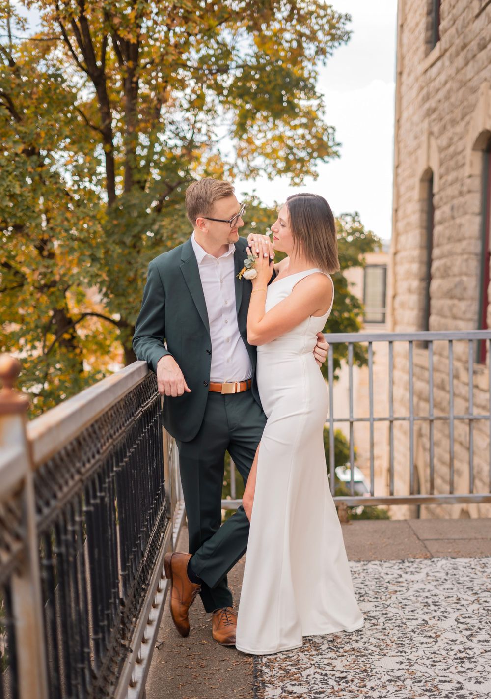 Bride and groom share a romantic moment on a stone balcony with colorful fall trees behind them.