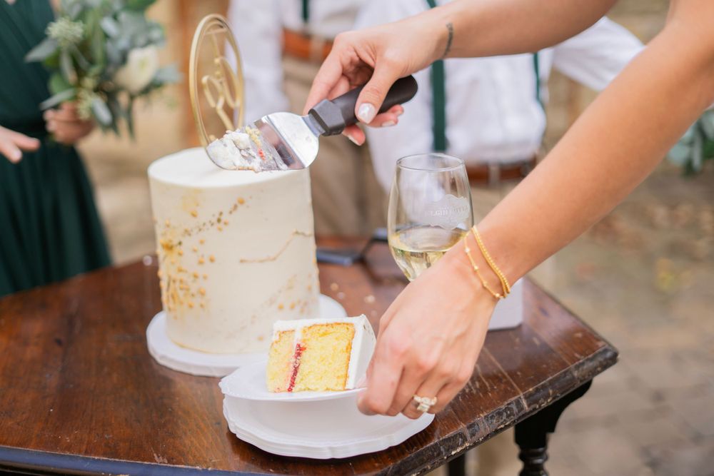 Newlyweds cut into a elegant white wedding cake with gold accents at their outdoor reception.