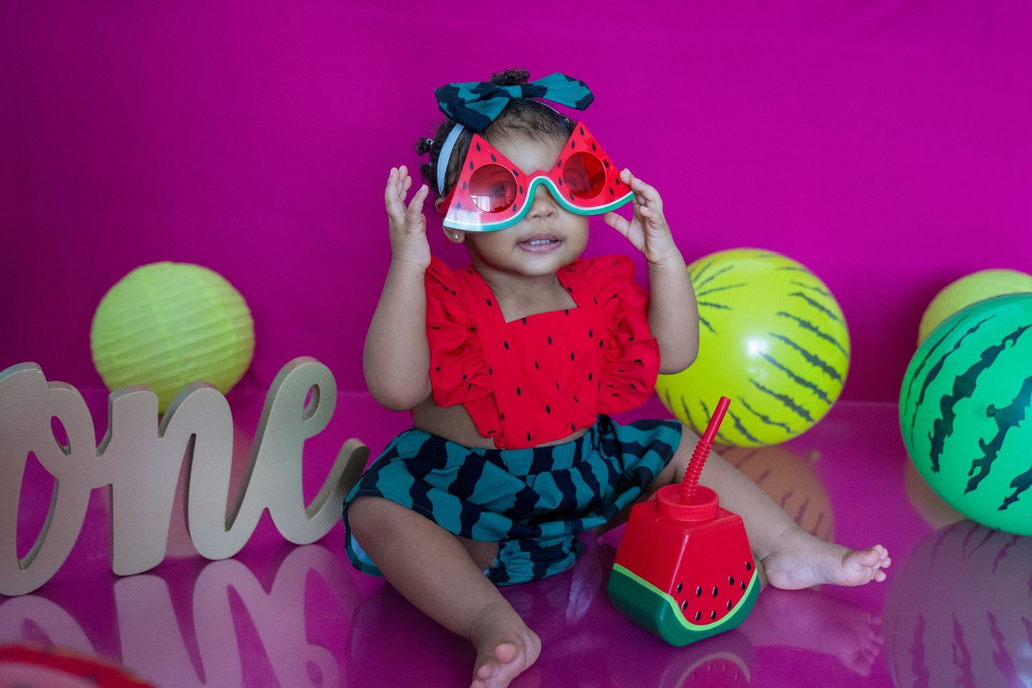 Colorful summer photo setup with watermelon prop and neon decorations against vibrant purple background.