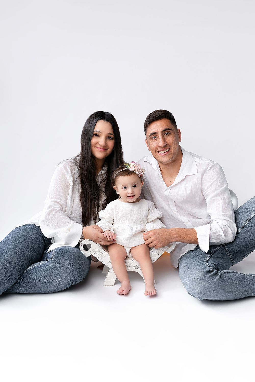 A family dressed in white and denim sits together on a white background for a minimalist portrait session.