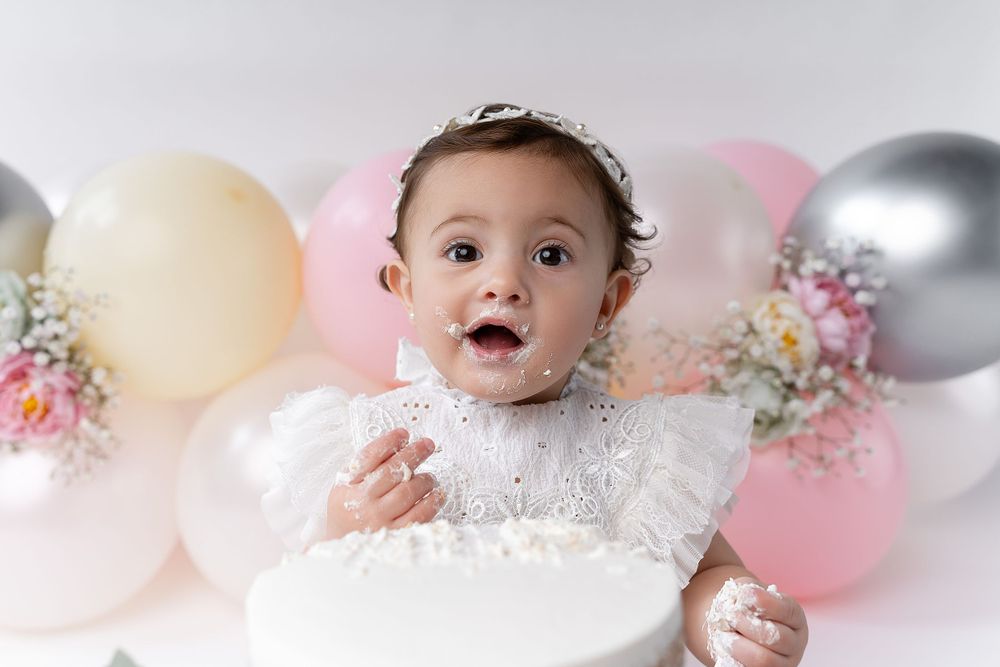Baby smiling with excitement during cake smash photo session with pink and silver balloon decorations.