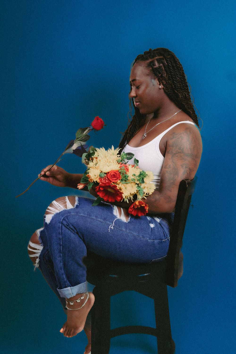 Creative portrait with person in casual wear posing with floral bouquet against blue backdrop.
