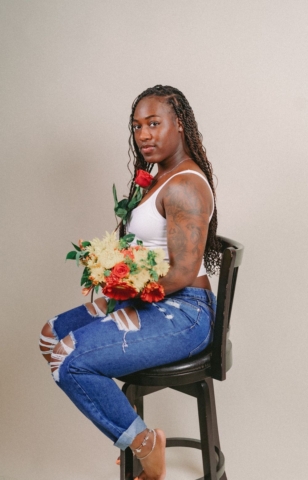 Studio portrait of person seated on chair holding colorful flower arrangement.