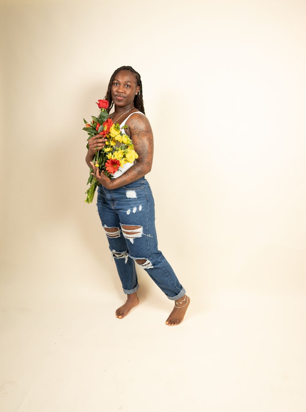 Casual portrait of person with flowers wearing distressed denim against neutral background.