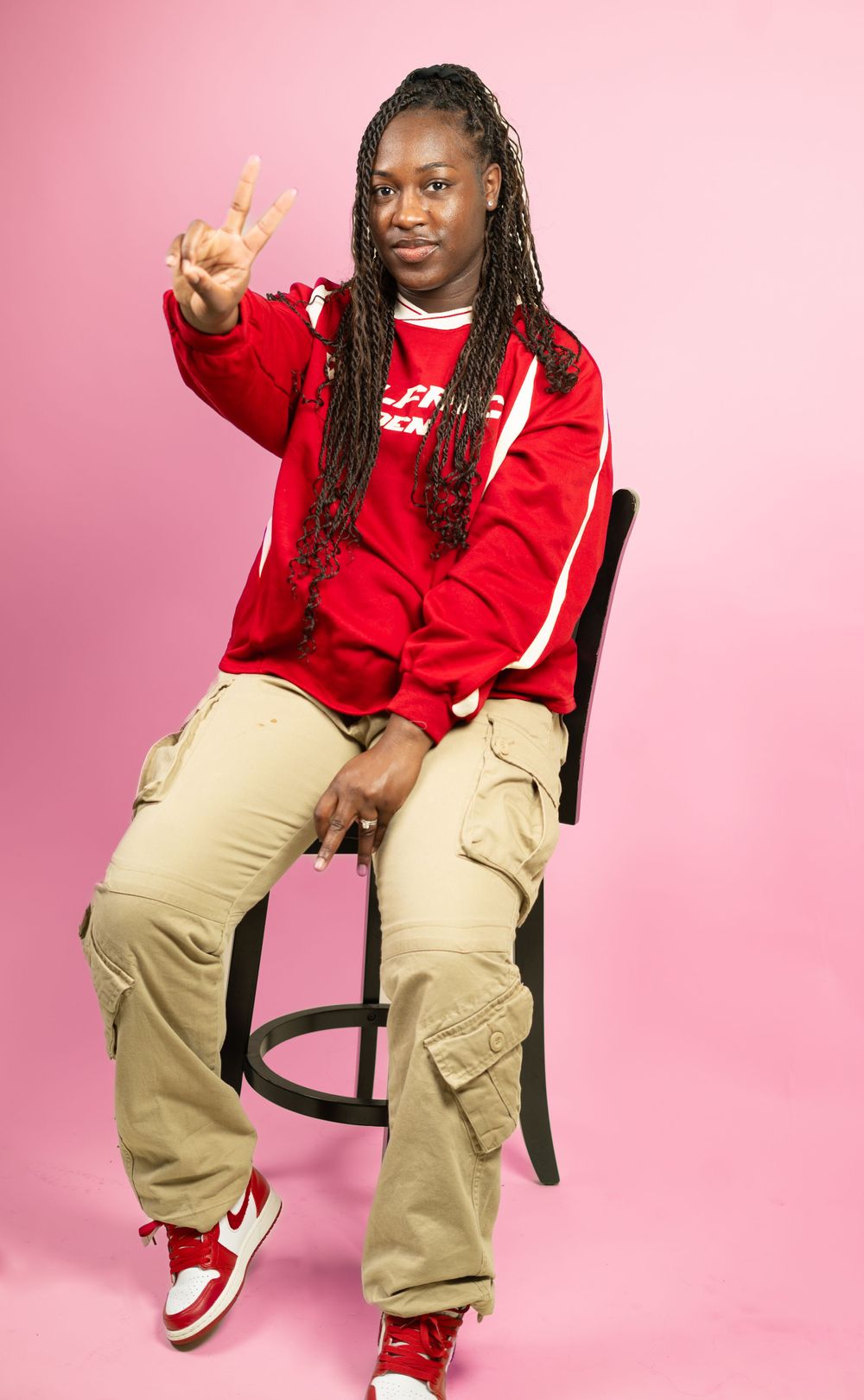 Model in red sweatshirt and khaki cargo pants poses against pink backdrop.