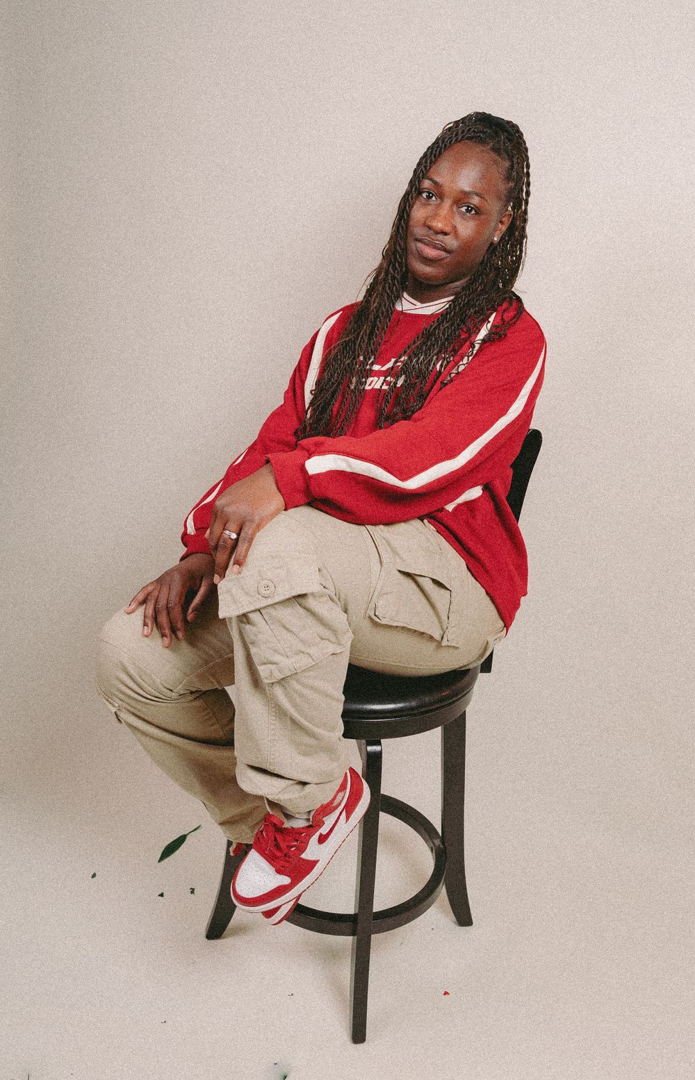 Model wearing red and white sweatshirt poses casually on black stool.