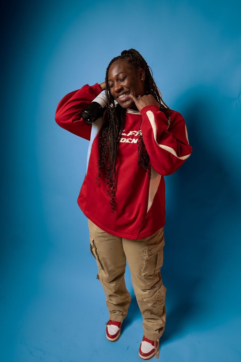 Person in red sweatshirt and khaki pants poses dynamically against blue background.