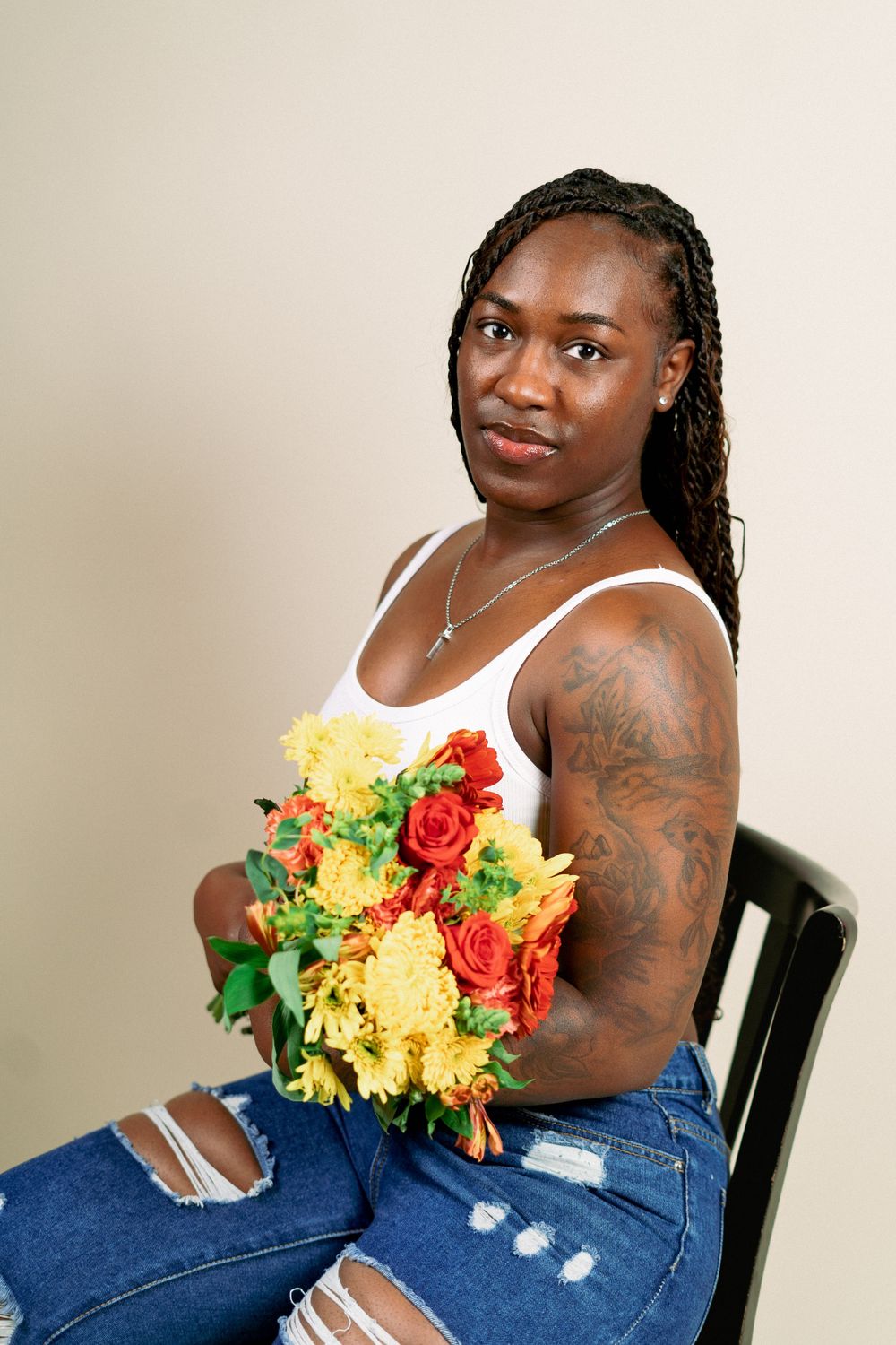 Portrait session with person holding vibrant yellow and red flowers while seated.
