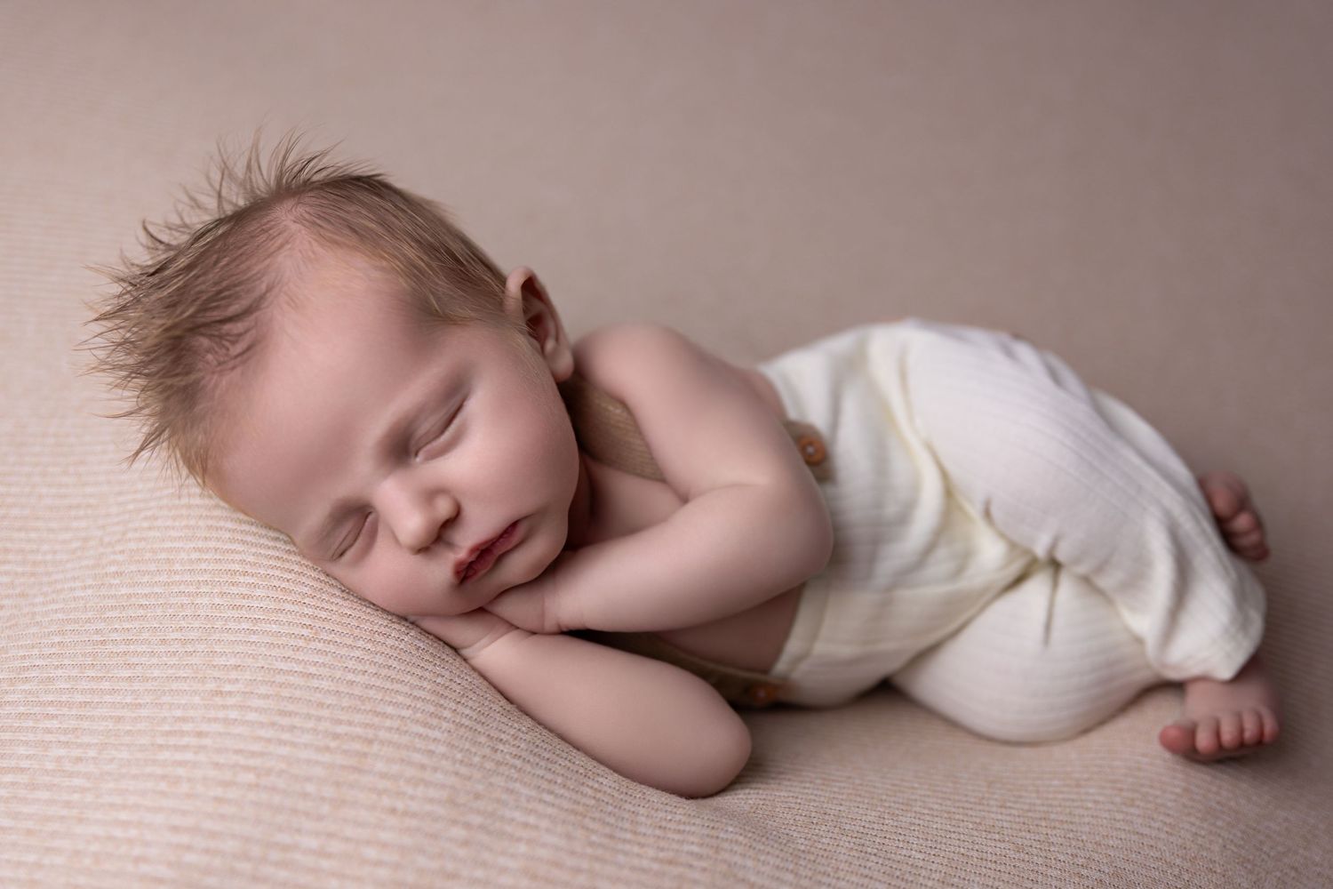 Sleeping newborn in pink blanket nestled in brown bucket on wooden floor with rustic backdrop.