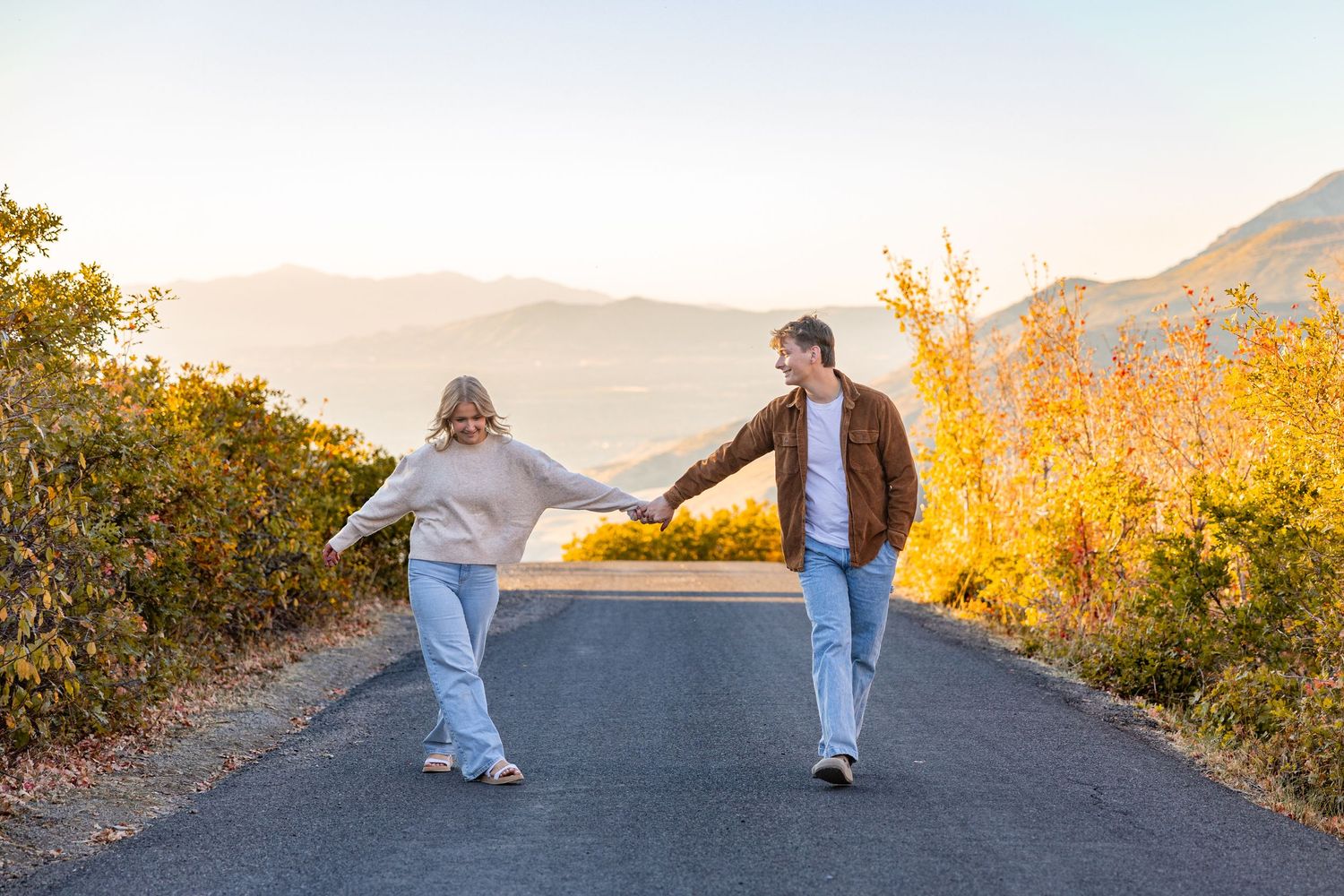 Couple walking on a mountain road during golden sunset with scenic mountain views.