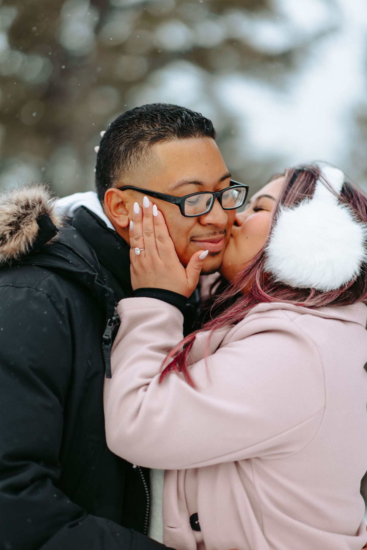 A couple shares a tender winter moment outdoors, wearing cozy jackets while sharing affection in the snow.