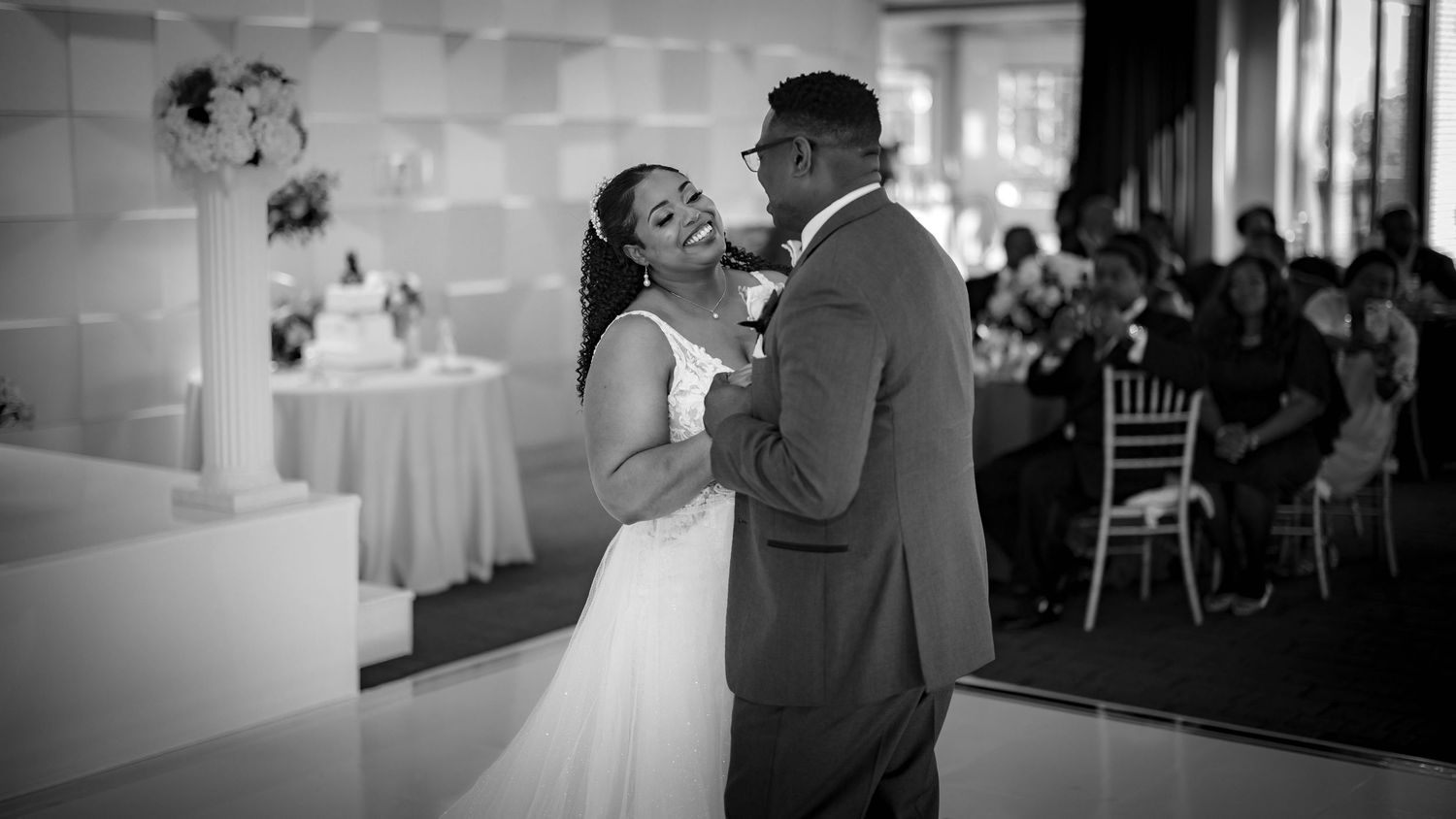 Two wedding guests share an intimate dance together in a reception venue with elegant white decor and chiffon chairs.