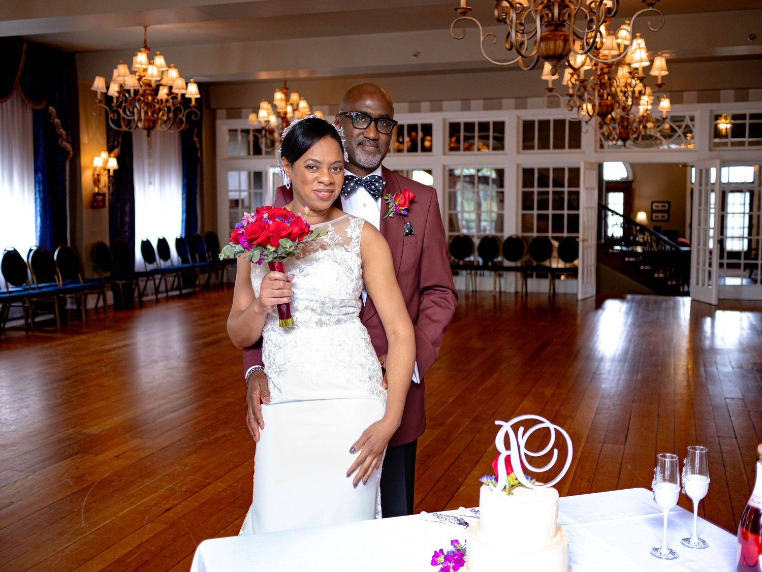 A couple celebrates their wedding day in an elegant ballroom with wood floors, chandeliers and a pink numbered centerpiece.