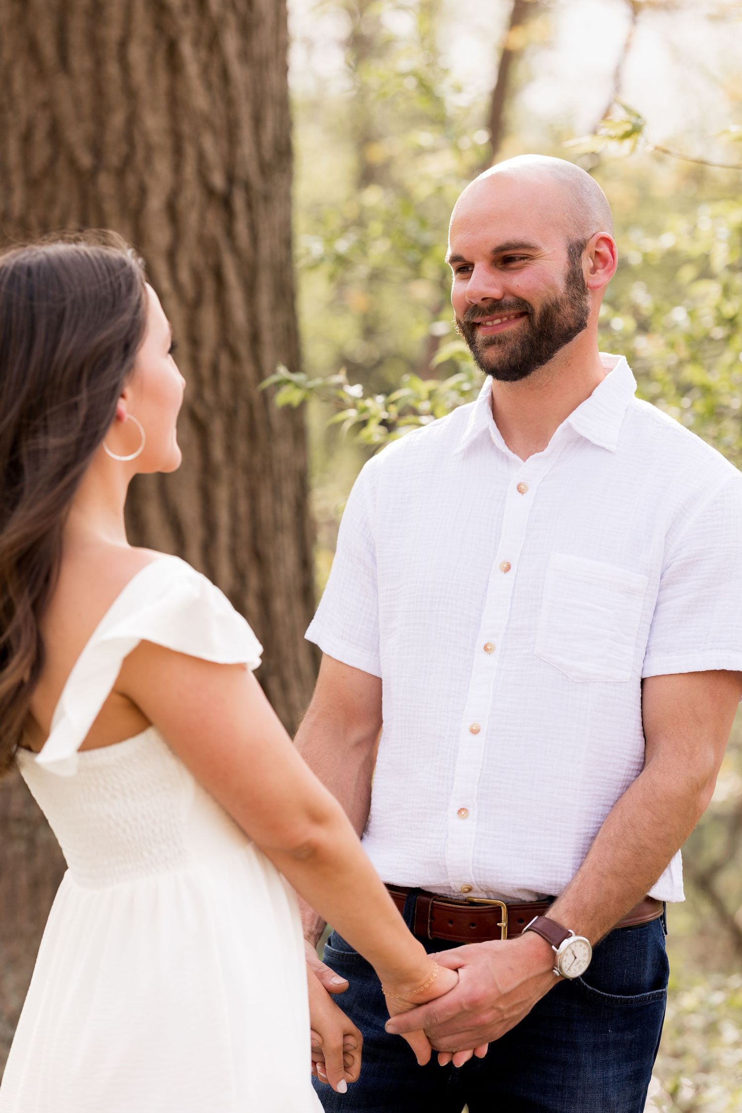 A couple shares a tender moment in casual attire against a wooded backdrop.