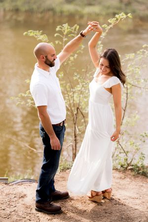 A couple dances together by a riverbank in coordinated white outfits.