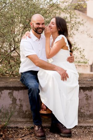 A couple shares a playful moment while sitting on a stone wall.