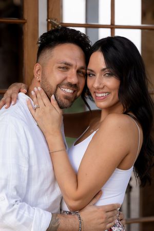 Couple in white clothing embracing and smiling in an indoor setting with natural light.