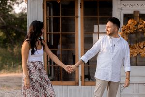 Couple in casual attire dancing and laughing together near rustic windows.