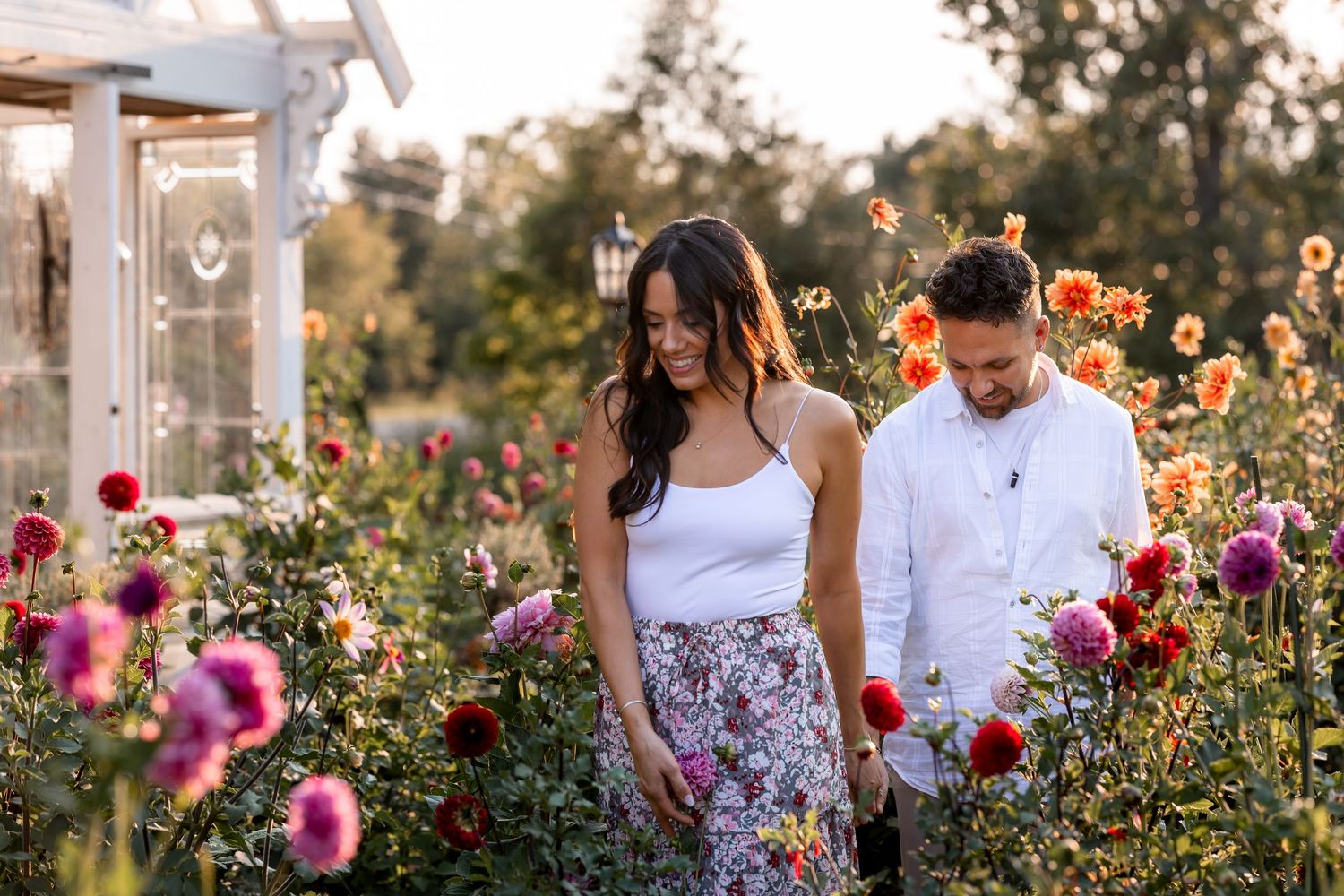 Romantic couple poses in a blooming garden with pink and purple flowers during golden hour sunset.