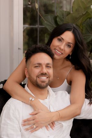 Couple shares tender moments in white outfits against a garden backdrop.