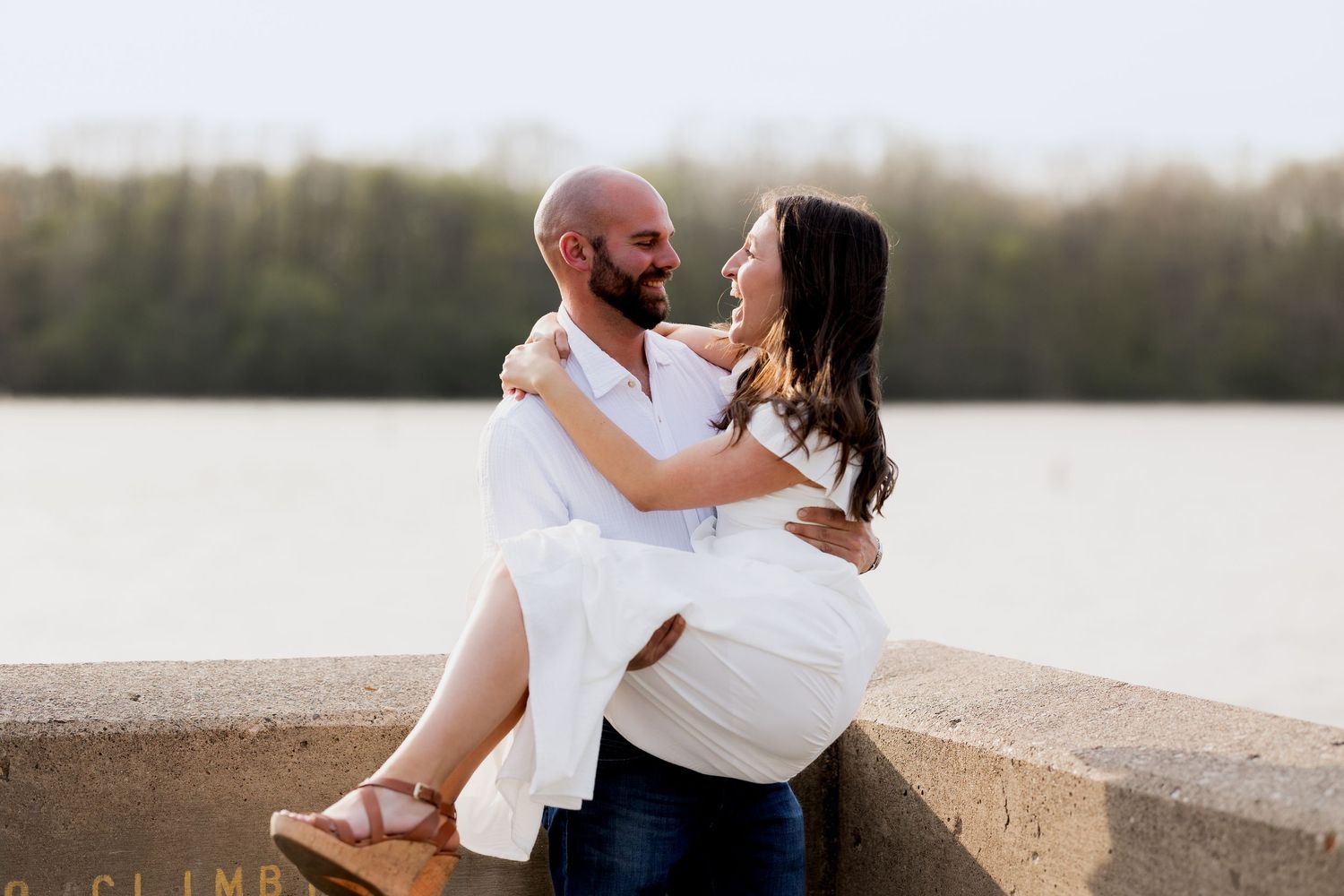 Romantic couple in white outfits sitting together on a beach at sunset.