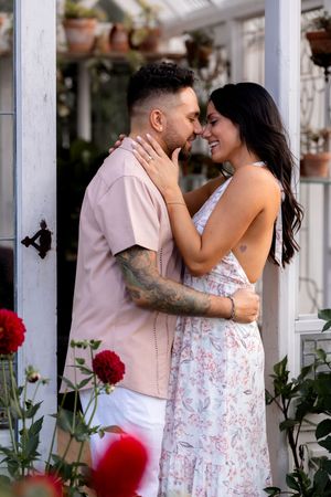 Romantic couple shares intimate moments against white garden trellis during photo shoot.