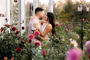 Garden photo session with couple among blooming roses and white architectural elements.