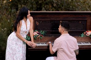 Romantic couple poses by an antique piano during an outdoor photoshoot.