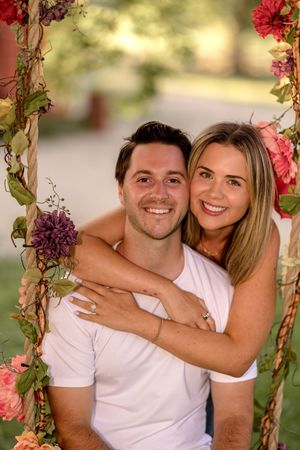Couple embracing on floral swing decorated with pink and purple blooms.