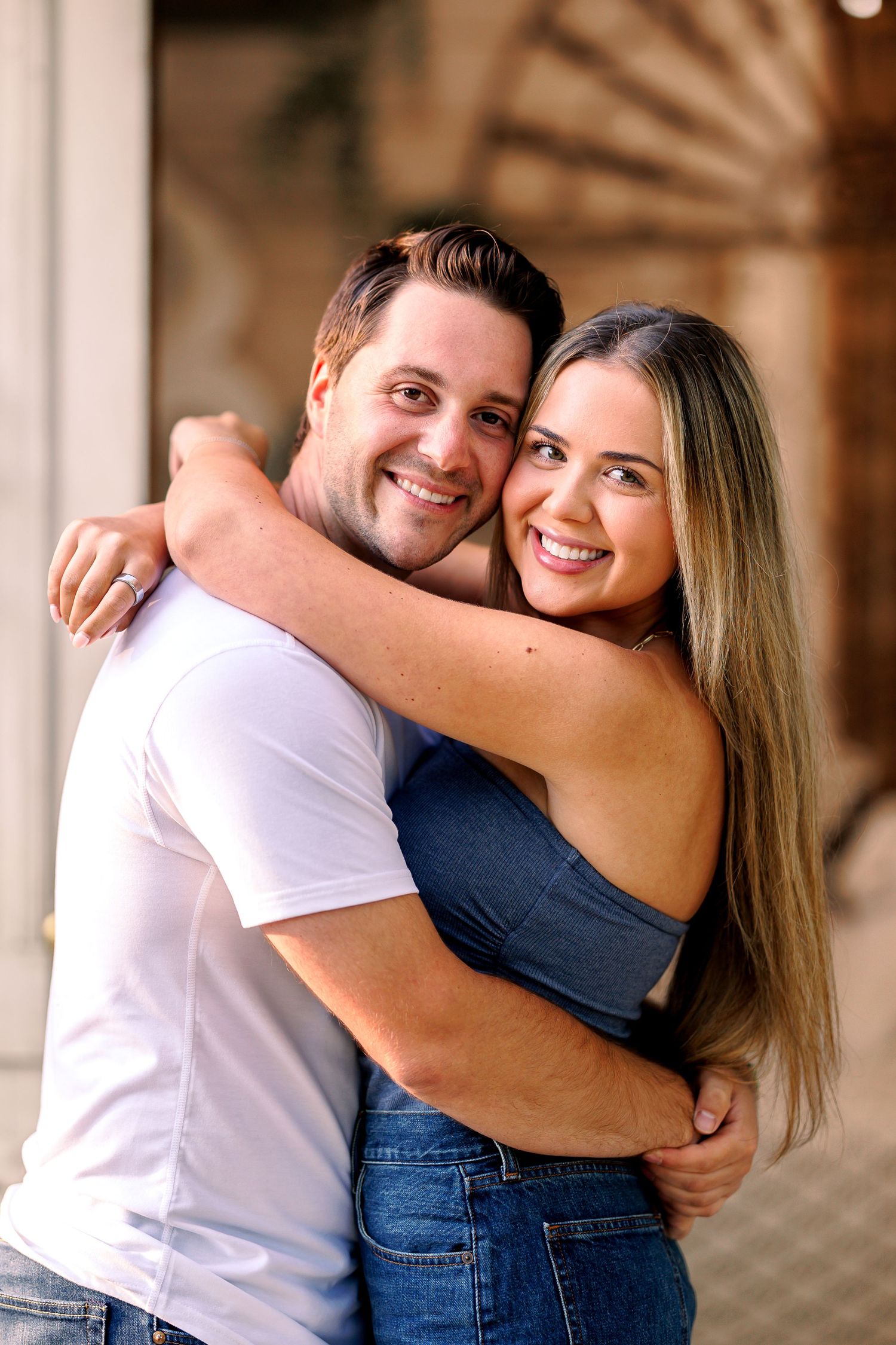 Casual couple sharing affectionate embrace against rustic backdrop.