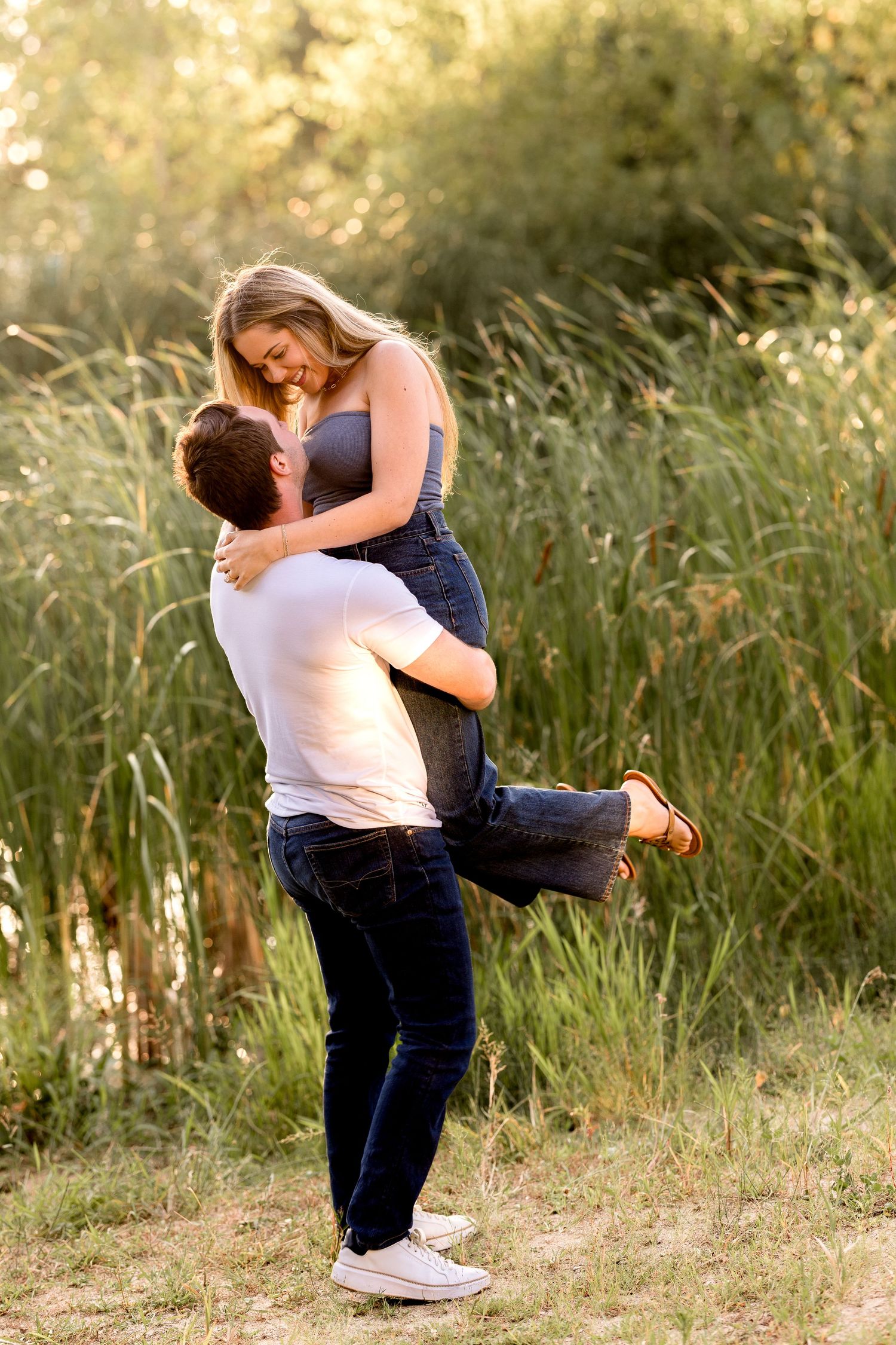 A romantic couple embraces in a sunlit field with tall grass during golden hour.