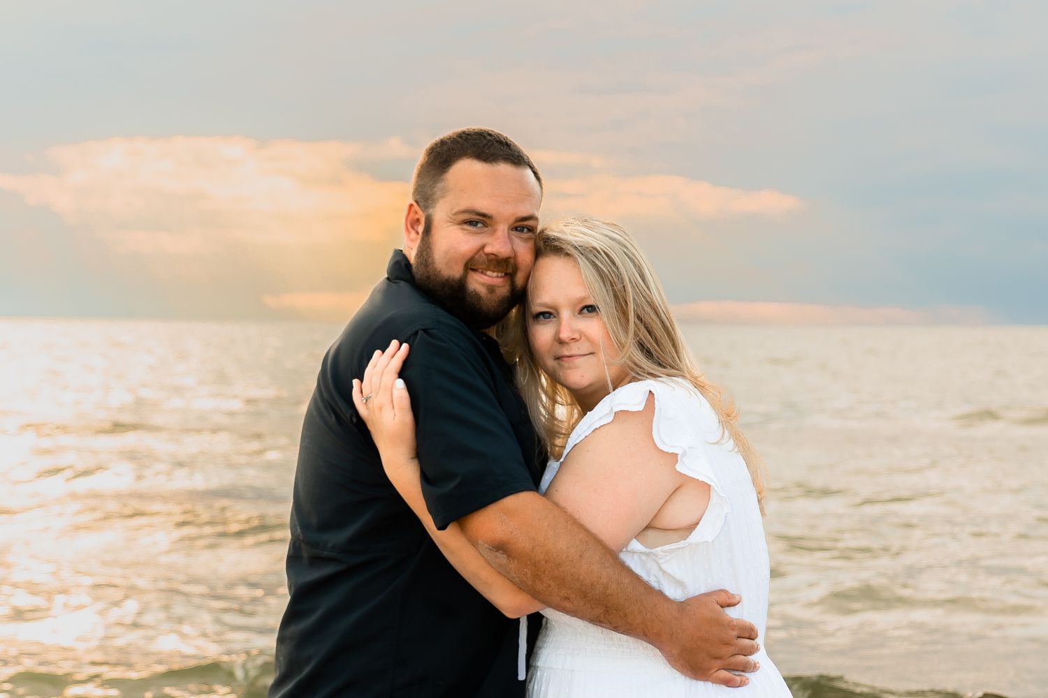 Couple shares intimate moments during beach photoshoot with dramatic cloudy sky.