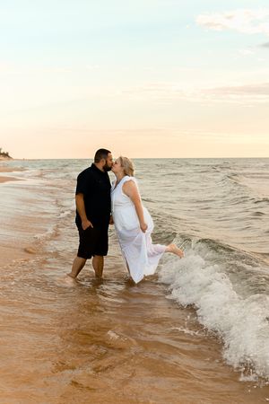 Playful couple splashes in ocean waves during sunset beach photography session.