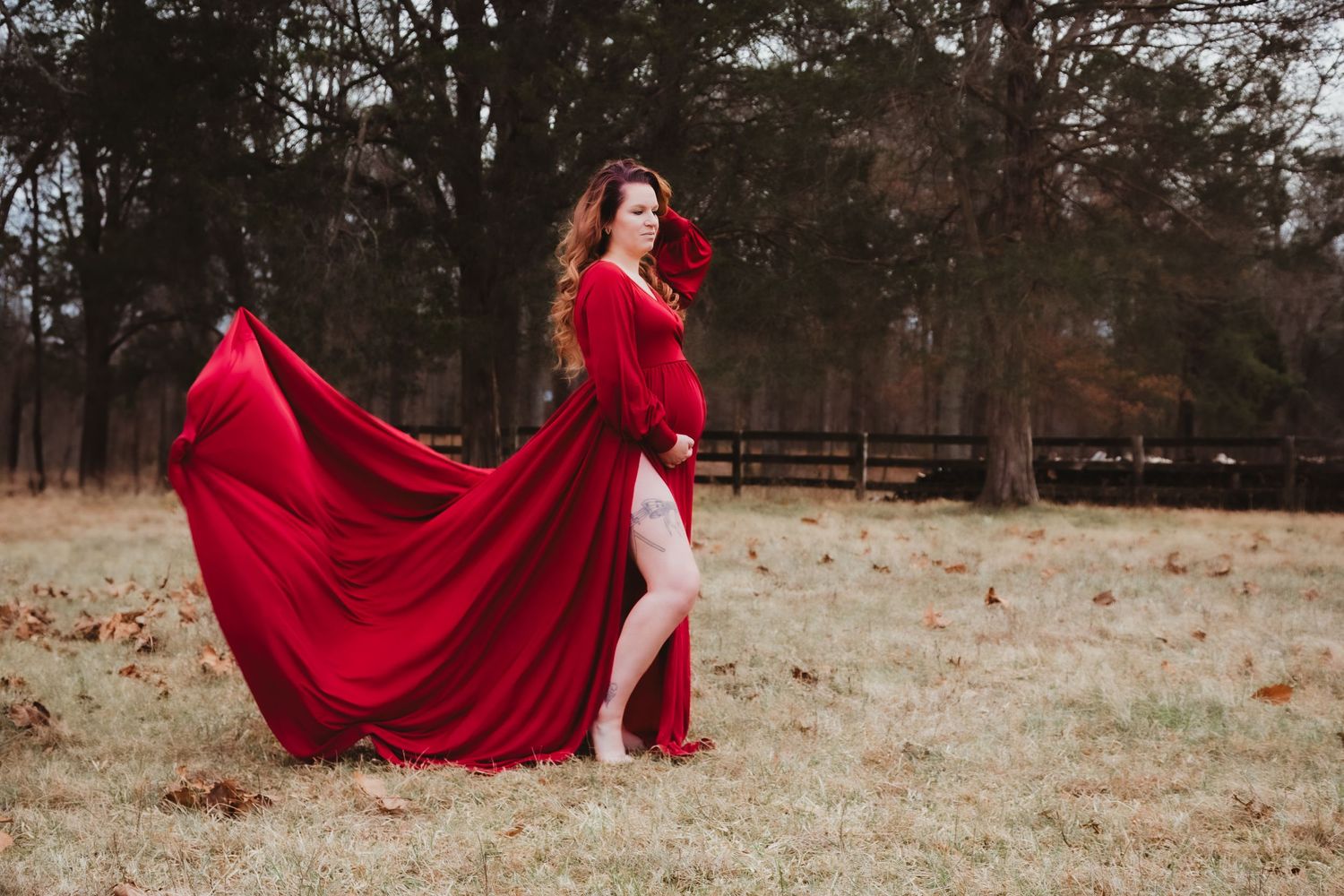 A flowing red gown billows dramatically in the wind on a misty autumn day in a rural field with fallen leaves.