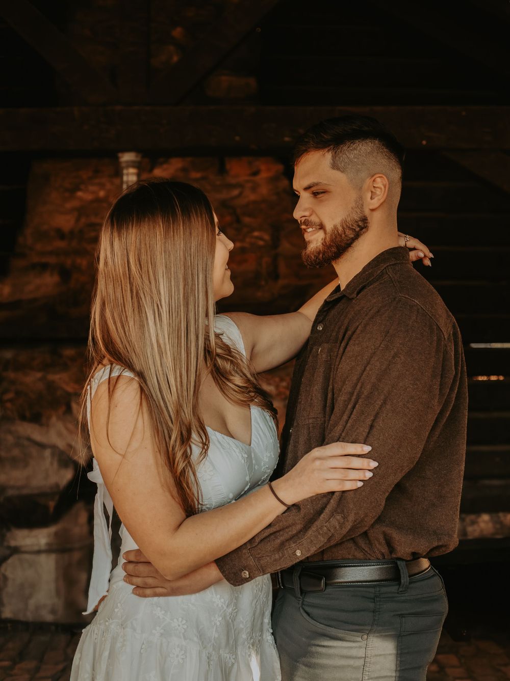 Romantic couple embracing in dim rustic setting wearing casual and formal attire.