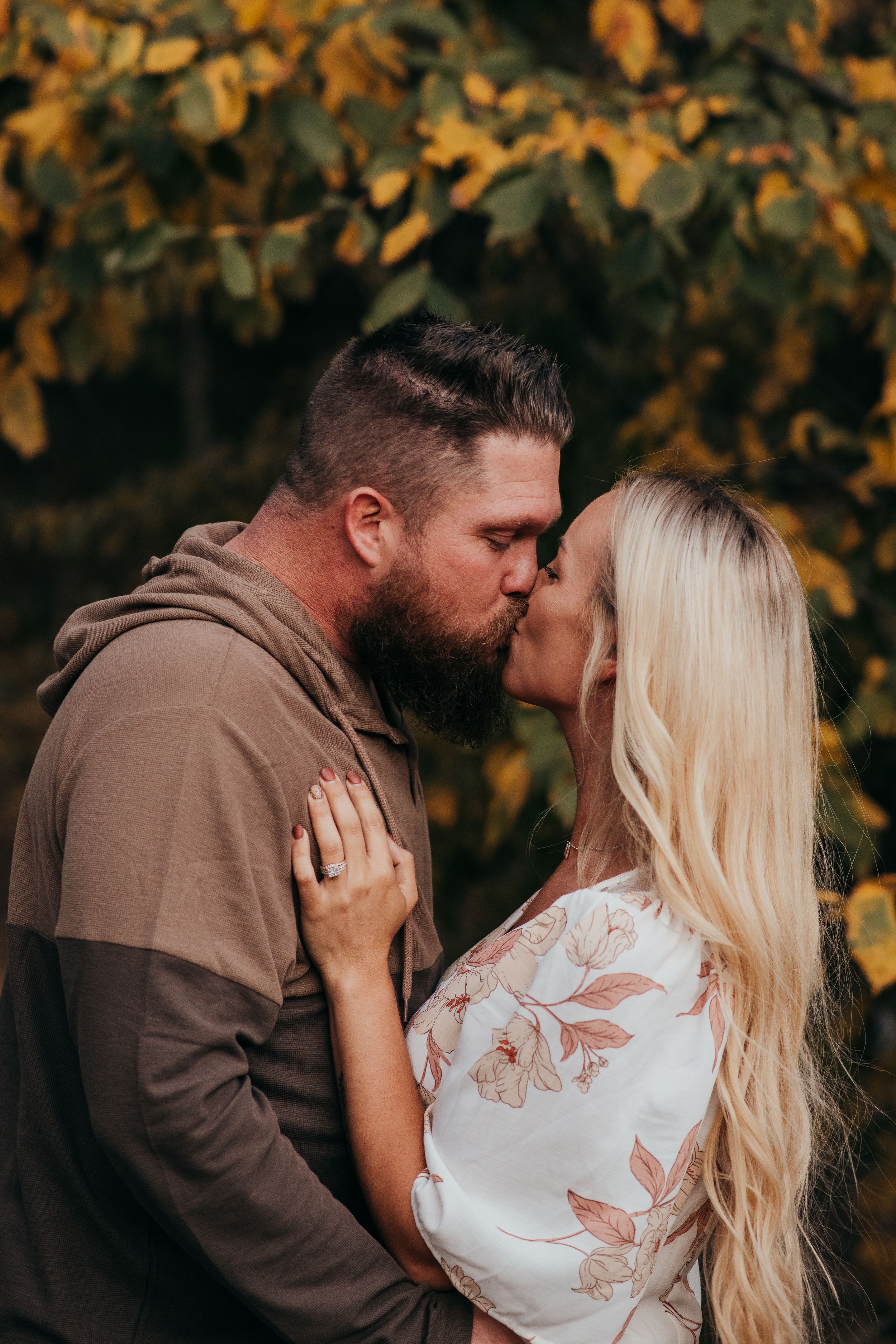 Intimate moment between couple against fall foliage background during engagement photoshoot.