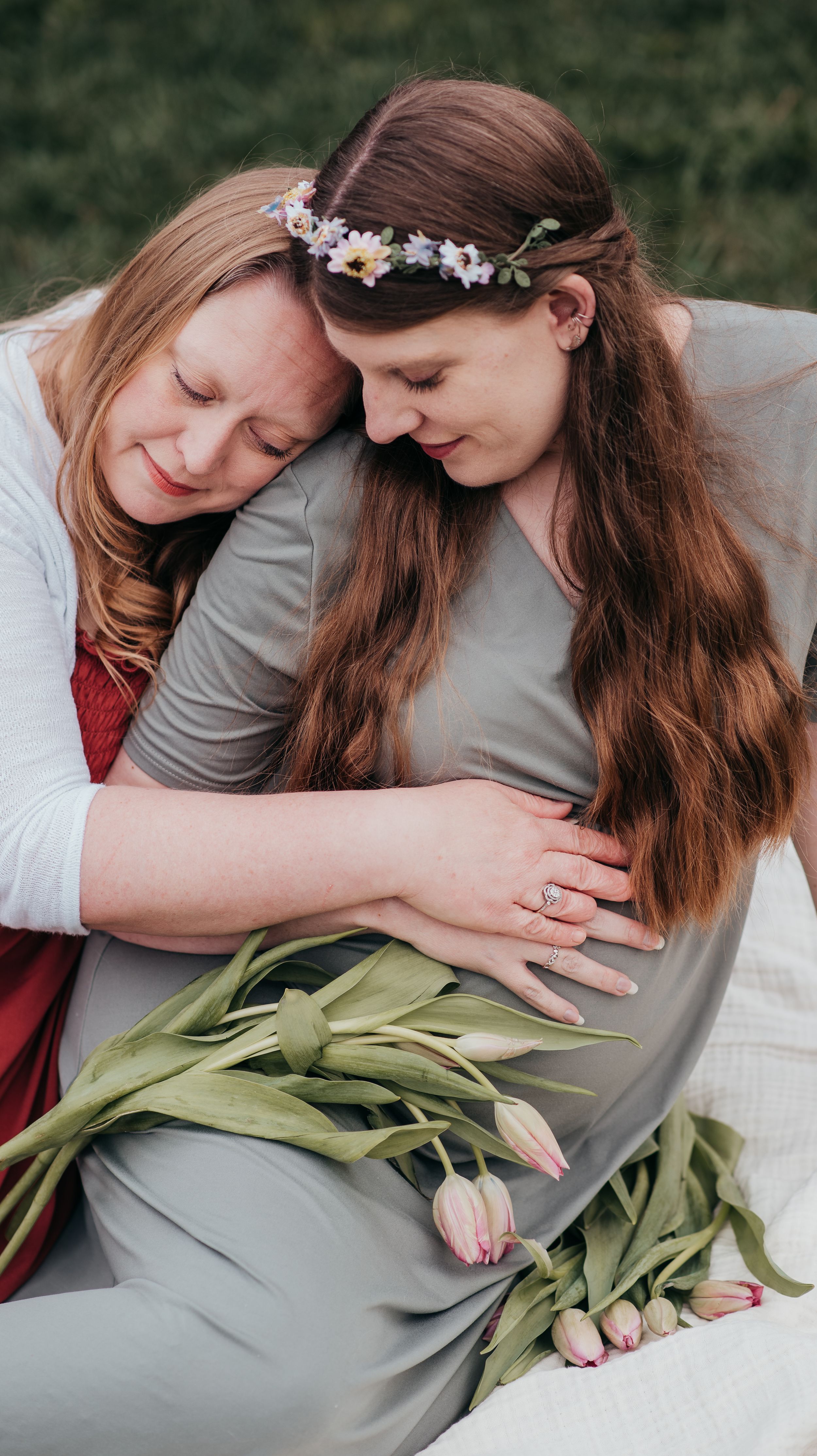 Two people in red and grey clothing share a tender moment outdoors with flowers and greenery.