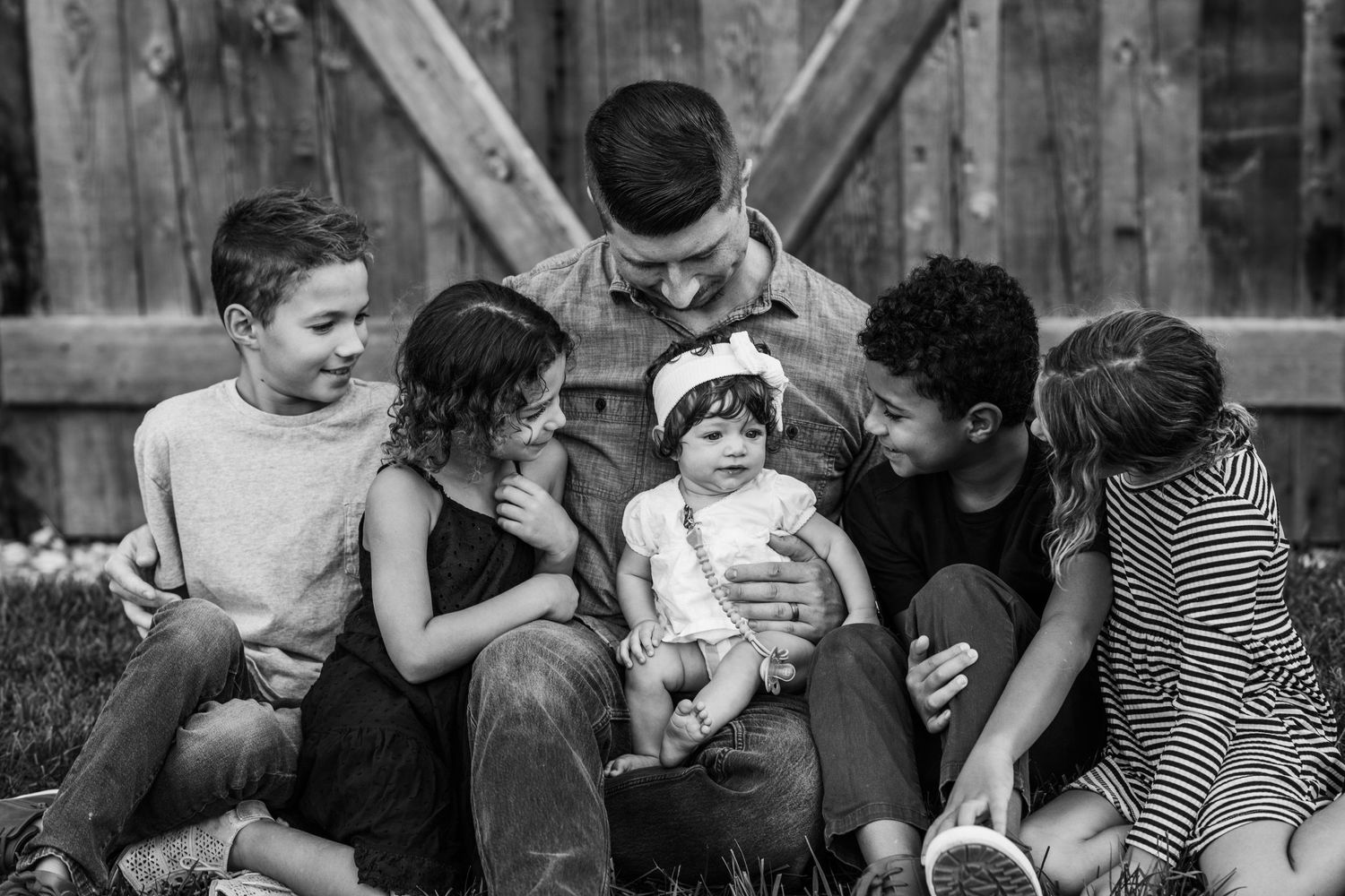 A black and white photo shows children sitting together outdoors sharing a tender moment in casual attire.