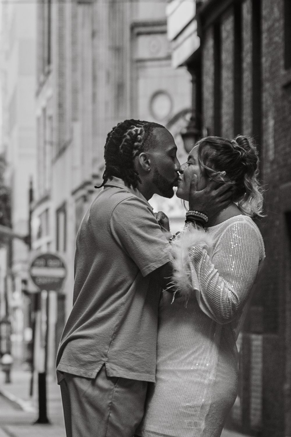 A couple shares a passionate kiss on a city street in a black and white urban portrait.