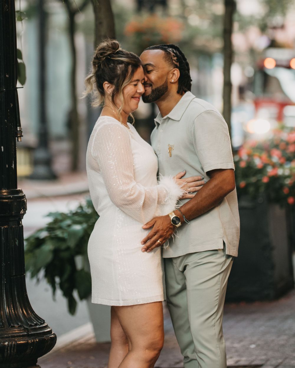 A couple shares a sweet moment as the man kisses the womans temple on a tree-lined city street.