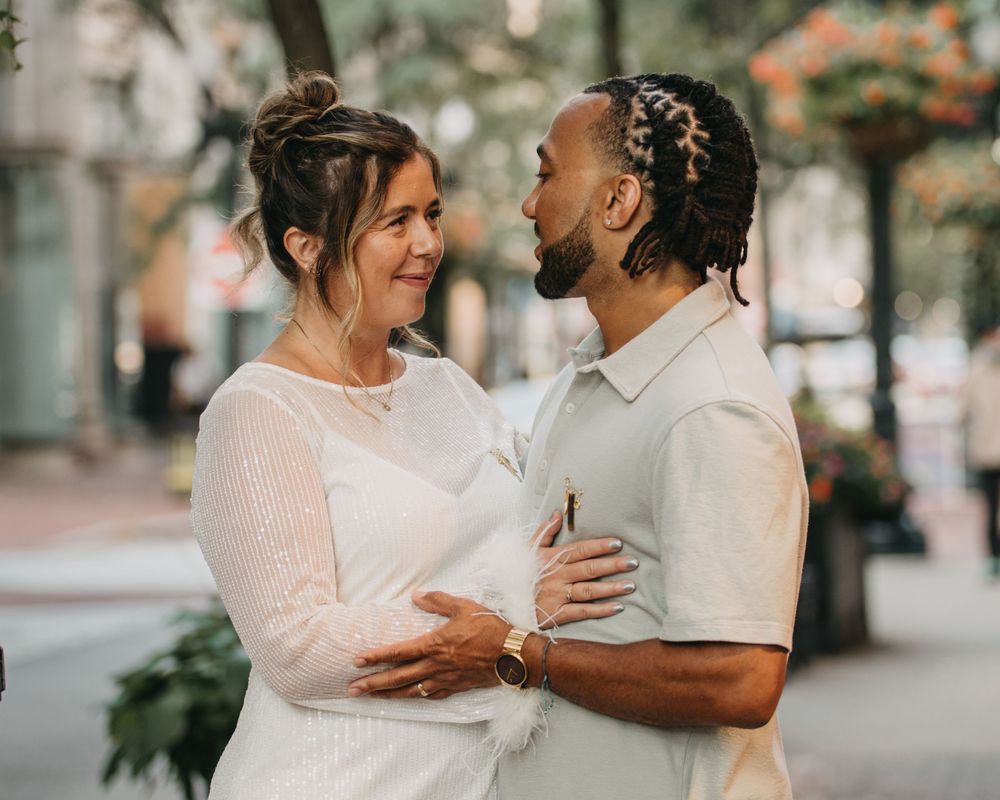 Couple in white and sage outfits gazing at each other tenderly during outdoor urban engagement session.