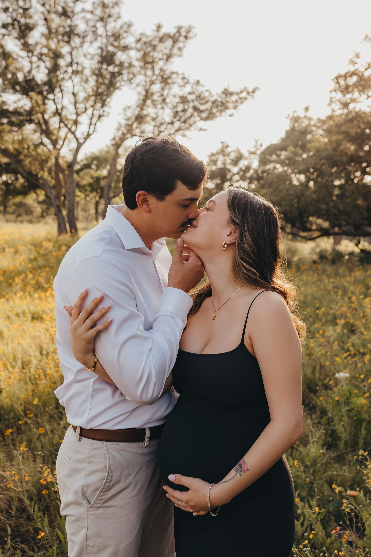 An expecting couple shares a romantic moment in a sunlit field during a maternity photoshoot.