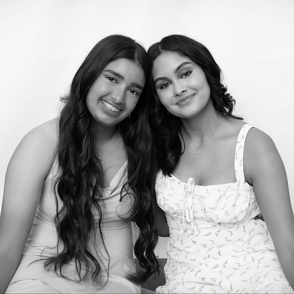 Black and white portrait series of two friends in white tops smiling and posing together in studio lighting.