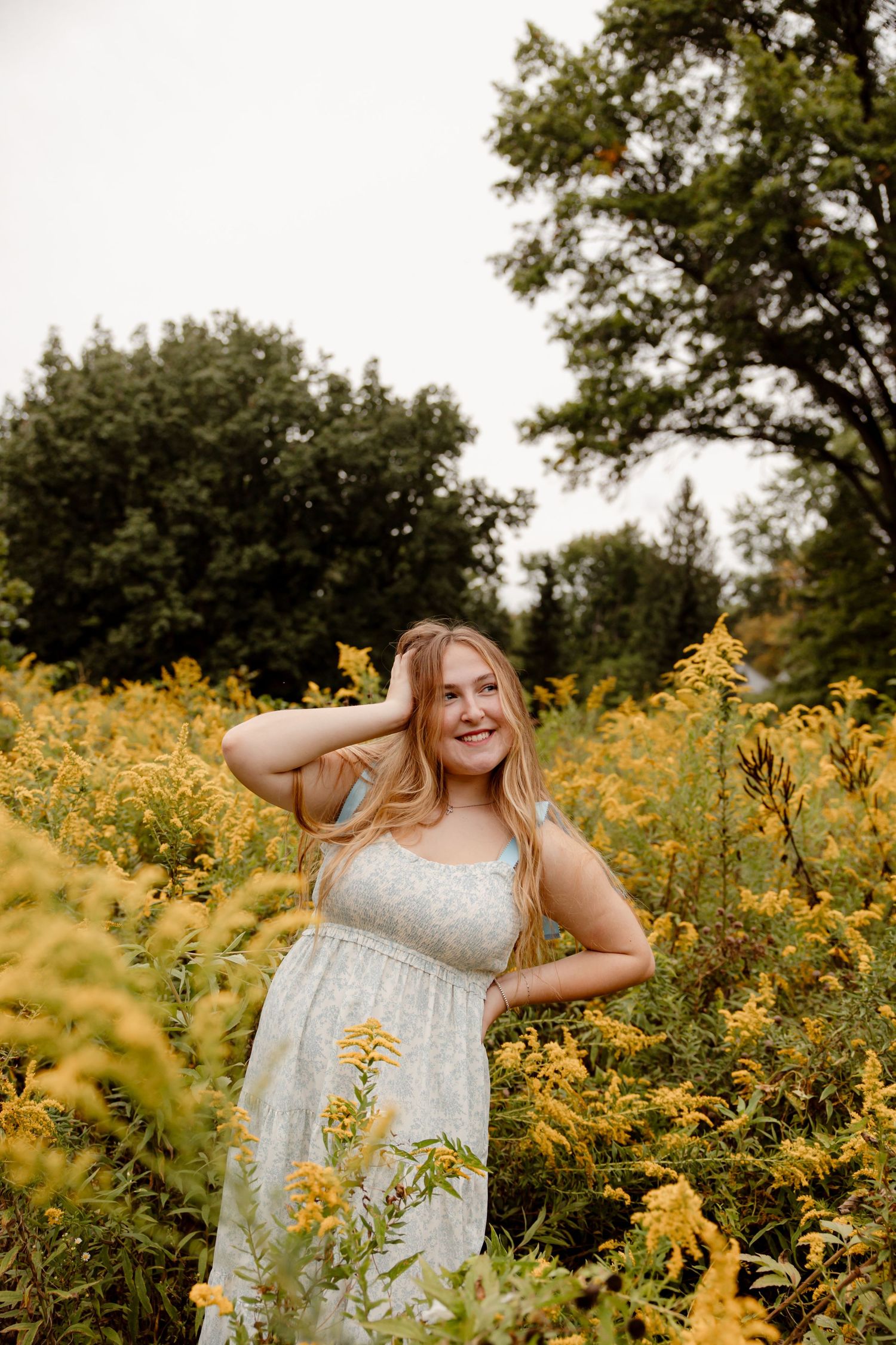 Woman in white dress standing among blooming yellow wildflowers.