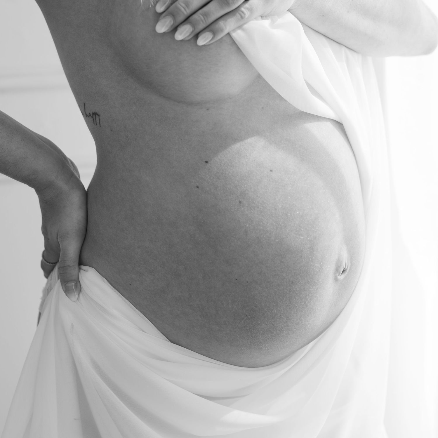 Black and white maternity photo showing pregnant belly against white fabric.