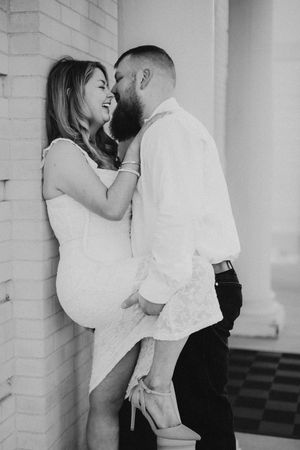 Black and white photo of a couple sharing an intimate moment against a white brick wall.