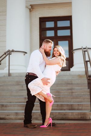 Playful couple posing on concrete steps in front of a classic building entrance.