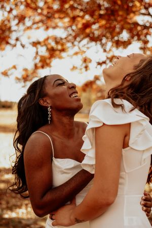 Two people in white ruffled outfits share a joyful embrace at sunset.