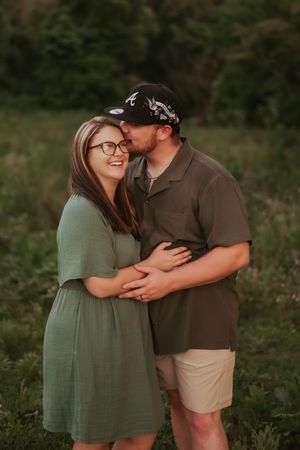 Romantic couple sharing tender moments in a grassy field wearing casual summer outfits.