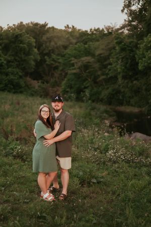A couple embraces in a green meadow at sunset during a romantic outdoor photoshoot.